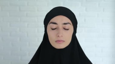 A beautiful Arab woman in a black hijab looks at the camera and starts to cry covering her face with her hands. Cruelty towards women in a Muslim family, strict rules of the Islamic world.
