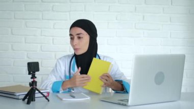 Muslim female doctor teaching at medical university remotely using webcam, online education. A medical college teacher trains future doctors and nurses. A doctor in a black hijab teaches students.