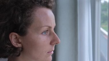 A woman standing at the window thoughtfully, attentively with a deep look, never blinking looks out the window. The woman has a beautiful, short haircut. A sad woman is waiting at the window.