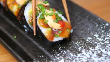 Close-up of Japanese rolls taking a piece with chopsticks. Japanese rolls wrapped in nori with rice and stuffing inside. Rolls with fish and seafood cut into small pieces convenient for eating.