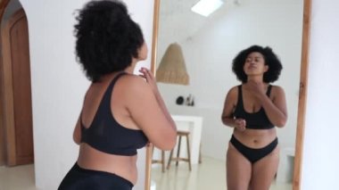 Multicultural plus size woman in lingerie looking at her body in the mirror. Black woman struggles with obesity and overweight, wants to lose weight and be slim Woman body positive without criticism