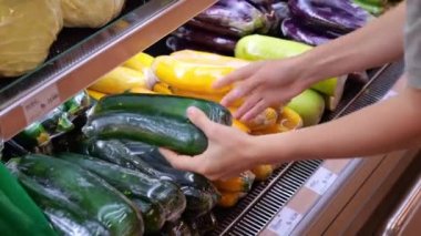 The woman takes zucchini from the shelf and selects the ripe ones. Buying vegetables at a local store. Consumption of vegetables is good for health food. Eco shop with organic vegetables.