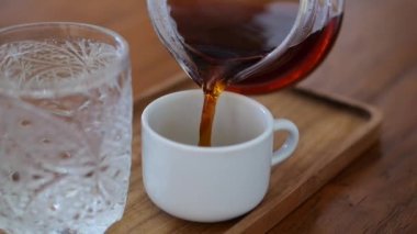 Black brewed tea is poured from a metal teapot into a white cup. Dolly effect. Close up. Slow motion. Tea ware in blur. Super Slow Motion Shot of Pouring Tea at 1000 fps.