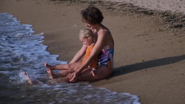 Little Blond Girl Sits Her Mothers Knees Sand Waters Edge — Stockvideo