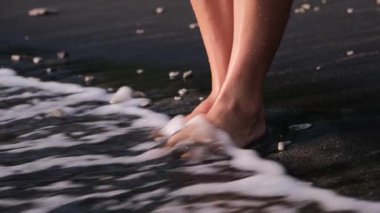 Womens legs without hairline, stand on the warm sand of the seashore. The rising water covers the legs above the ankle. Water washes away and takes away bad emotions, giving relaxation in return.