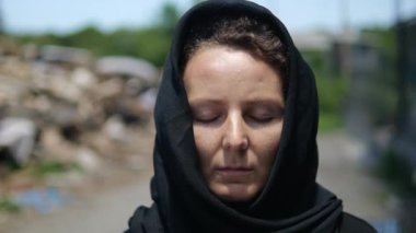 The face of a woman left a widow close-up. She stands against the backdrop of a destroyed building, silently praying and mourning for her loved ones who died. Consequences of the war.