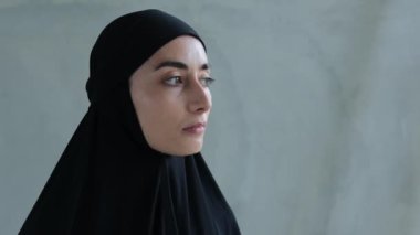 A woman in a black hijab looks to the side with apprehension, afraid of punishment for violating Sharia law, the hard life of Islamic women who are limited in their freedoms in Muslim families.