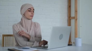 A Muslim woman can work in the office, freedom of choice of work for Muslim women. A beautiful woman in a hijab sits at a computer and looks at the camera. New realities of the Islamic world.