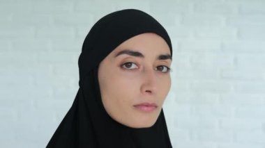 Beyaz tuğladan bir duvara yaslanmış siyah tesettürlü bir Arap kadının yüzünü yakından çek, kafasını çevirir ve kızgın bir bakışla kameraya bakar. Müslüman kadınların teröristler tarafından işe alınması.