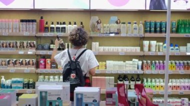 A woman buys cosmetics in an eco store that sells ethical cosmetics and body care products, there are plastic bottles of various colors from natural ingredients. Ubud - Indonesia - 2022
