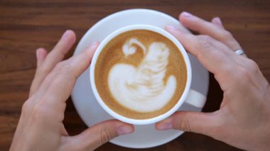 Kadın eli tarafından tutulan bir kupa mis kokulu kahve. Ahşap bir masada, beyaz bir kupadan sabah sampuccinosu içen bir kadın. Kahve içmek vücudu ve ruhu canlandırır..