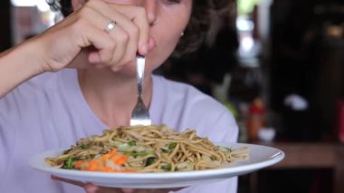 A young Italian woman eats delicious spaghetti from a plate in a restaurant, wraps pasta on a fork and puts it in her mouth with pleasure. Lunch at an Italian restaurant for the whole family.