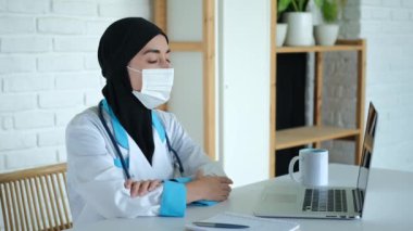 İslam dünyasındaki kadınlar için bir hastanede çalışmak. Siyah peçeli bir sağlık görevlisi ve iş yerindeki tıbbi önlüklü hastaları kliniğe kaydetmek için dizüstü bilgisayarın bulunduğu bir masada oturuyor..