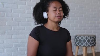 Afro woman in headphones in front of a laptop is meditating online. Harmonious work with oneself, curing mental illness and anxiety through meditation. A black meditates on a purple mat.