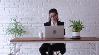 The office employee looks immaculate. The design of the office is made in a modern style. Decor flowers. The employee herself decided to rest, putting her feet on the table and drinking a drink.