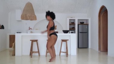 African American model plus size dancing at home in the kitchen in black lingerie. The woman does not pay attention to excess weight. An overweight woman loves and accepts herself.