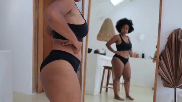 一位身穿黑色女士内衣的非洲裔美国妇女在镜子前看着她的曲线身材 她喜欢她的身体 妇女对肥胖的接受程度 身体正性的概念 — 图库视频影像