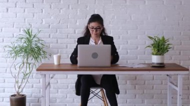 At the workplace at a table, an employee dances inspired while doing her job. Throws away an empty glass of coffee and types on a laptop while continuing to dance in a chair. Funny office plankton.