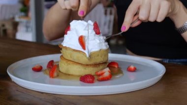 Dessert is served on a beautiful white plate, a cake with caramel and strawberries. On top is a fluffy hat made of cream decorated with a mint leaf. A woman cuts a cake in half