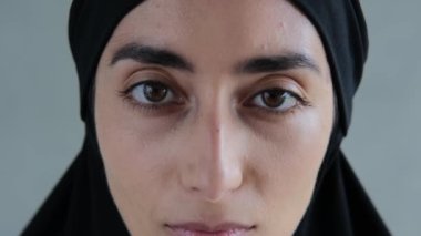 An Arab woman. The head is covered with a black hijab. The hijab hides her hair beauty. The face is oval, the eyebrows are thick black, the woman has large almond-shaped eyes.