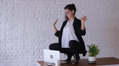 In the functional area, an office employee dressed in a business style relaxes freely in dance movements. The girl dances on a working office table, scatters papers. Cheerful office plankton.