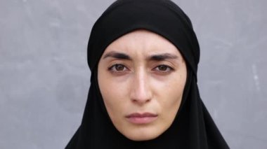 Yakın çekim, Müslüman ülkesindeki baskıcı feminist kadının yüzü. Esmer, tesettürlü bir kadın kameraya ağır, üzgün, ciddi bir bakışla bakıyor. Kahverengi gözlü İslami kadın kameraya bakıyor.
