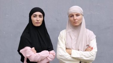 İki ciddi, somurtkan Müslüman kadın kollarını göğüslerine kavuşturup kameraya bakıyor. Türban takan kararlı ve kendinden emin feminist kadın aktivistin portresi.