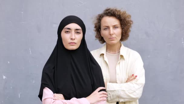 2人の女性の手で カメラをじっと立って折り畳まれた ヒジャーブとヨーロッパの白人女性における東洋のムスリム女性の肖像画 人種や宗教に関係なく二人の女性の友情 — ストック動画