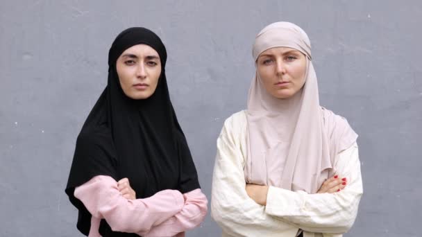 两个严肃皱着眉头 头戴伊斯兰头巾的穆斯林妇女抱着胳膊站在胸前看着镜头 头戴头巾的坚定而自信的伊斯兰女权运动者的画像 — 图库视频影像