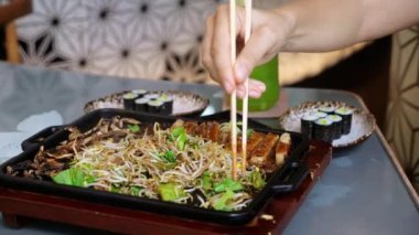 İki Çin yemek çubuğuyla kadın eli iştah açıcı bir vejetaryen yemeği karıştırır: sıcak enoki mantarı, avokado ve sos. Masanın üzerinde avokado dilimleri ve Norveç yaprağında Çin pirinci var..