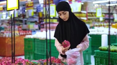 Geniş bir süpermarkette çalışan genç Müslüman kadın, Pitaya 'yı küçük bir torbaya koyar ve olgun bir ejderha meyvesi seçer. Meyvenin orijinal görünüşü onu almanızı ve alışılmadık tadı denemenizi teşvik eder..