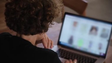 Kameraya arkası dönük beyaz bir kadın kişisel bir bilgisayarda çalışıyor. Bir kadın tasarımcı, moda endüstrisindeki internet sitelerine ve mağazalara kıyafetlerle göz atar, moda eğilimlerini analiz eder.
