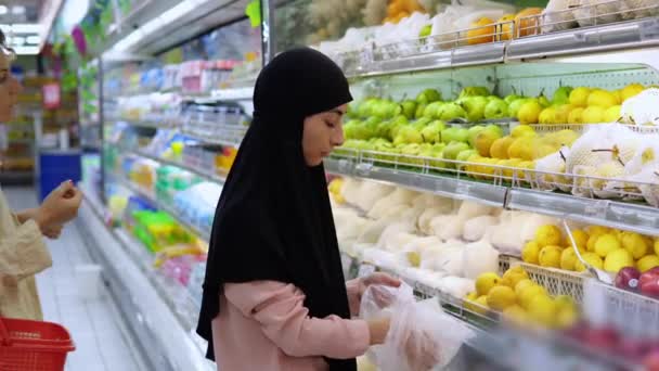 히잡을 여자는 비닐봉지에 과일을 모은다 슈퍼마켓의 진열대에 쇼핑객 택한다 건강하고 — 비디오