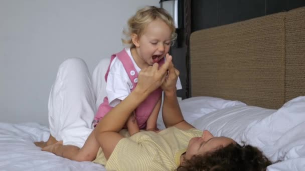 慢动作 母亲和孩子在床上玩耍 在一起度过时光 女人和女儿在家里玩得很开心 孩子坐在妈妈的肚子上 一个女人躺在床上 — 图库视频影像