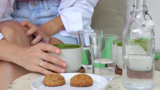 緑豊かなおいしい香りの抹茶とオートミールクッキー 白人の巻き毛の女性が外で抹茶を飲み さわやかな朝の天気を楽しんでいます 自然の中でおいしい朝食 — ストック動画