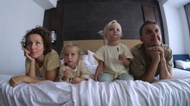 Kızları olan aile televizyon, televizyon izliyor, evde film seyrediyor ve geniş yatakta uzanıyor. Eşler, ebeveynler film izler, çocukları yatakta yatarken televizyonda çizgi film izlerler. Bütün aileyle çizgi film izlemek..