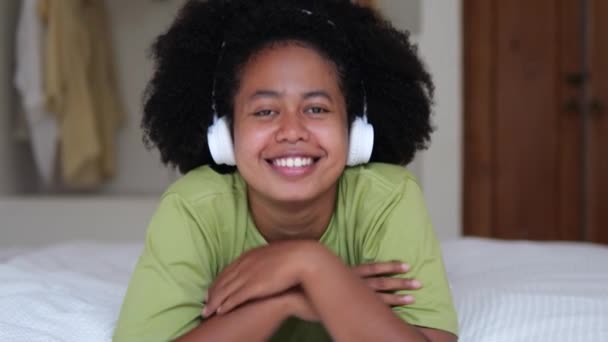 Yatağında Kulaklıkları Olan Çekici Kıvırcık Saçlı Siyah Kız Kameraya Bakarken — Stok video