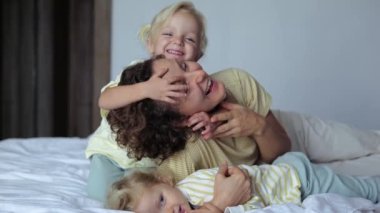 Çocuklar ve annem yatakta uzanıp gülüyorlar sarılıyorlar ve birlikte iyi vakit geçiriyorlar. Mutlu çocukluk kavramı sevgi dolu, neşeli ve nazik bir annenin yanında geçiyor. İki beyaz kızın mutlu çocukluğu..