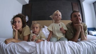 Kızları olan aile televizyon, televizyon izliyor, evde film seyrediyor ve geniş yatakta uzanıyor. Eşler, ebeveynler film izler, çocukları yatakta yatarken televizyonda çizgi film izlerler. Bütün aileyle çizgi film izlemek..