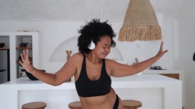 Neşeli, mutlu, Afro-Amerikan iç çamaşırlı çekici zenci kadın evinde enerjik bir şekilde dans ediyor. Afro-Amerikalı kadın dans ediyor, kulaklıkla müzik dinliyor ve hayattan zevk alıyor.