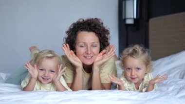 Anne ve bebekler peekaboo oynuyor ve eğleniyorlar. Önden bakan mutlu kadın, bebek kızlarla yatakta 