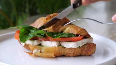 Yakın plan, bıçak ve çatalla, eller mozzarella, domates, fesleğen yapraklı kruvasan. Alışılmadık bir tadı olan lezzetli besleyici aromatik yemek. Lezzetli yemekler servis eden tabak restoranındaki kruvasan.