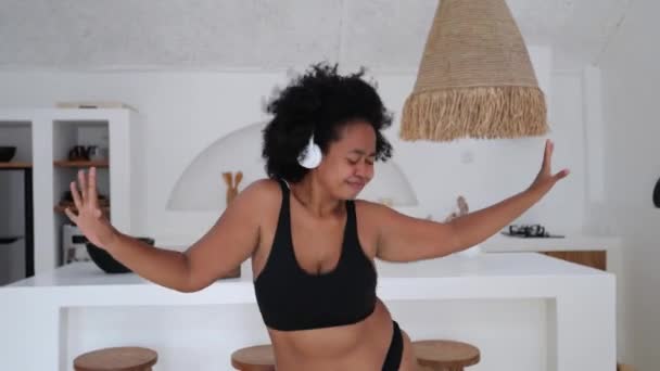 明るく幸せな魅力的な黒いアフリカ系アメリカ人の女性の下着を精力的に自宅でアパートで踊っている アフリカ系アメリカ人の女性が踊り ヘッドフォンで音楽を聴き 人生を楽しむ — ストック動画