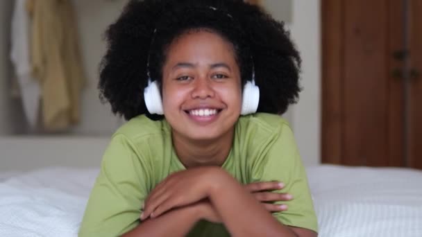 Vonzó Göndör Hajú Fekete Tini Lány Fülhallgatóval Ágyon Nevet Mosolyog — Stock videók