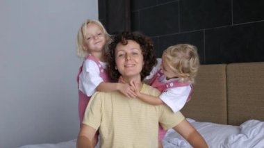 Çekici kıvırcık saçlı beyaz kadın gülüyor ve gülümsüyor, iki kız çocuğu annelerine her iki taraftan sarılıyor. İki tatlı çocuğu olan mutlu, sevgi dolu bir anne. İki ikiz kız annelerine sarılır.