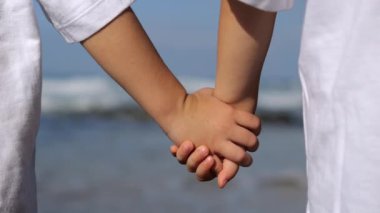 Denizin kıyısındaki çocukların duygusal açıdan sakin ve sakinleştirici fotoğrafları. İki küçük çocuk deniz kıyısında el ele tutuşmuş. El ele tutuşan 6-10 yaşındaki çocukların bronzlaşmış ellerine yakın durun..