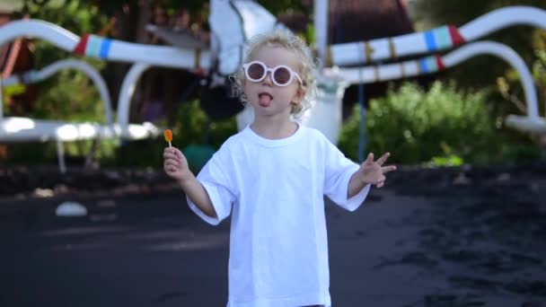 Vtipná Holčička Brýlemi Ukazuje Jak Její Jazyk Drží Lízátko Ruce — Stock video