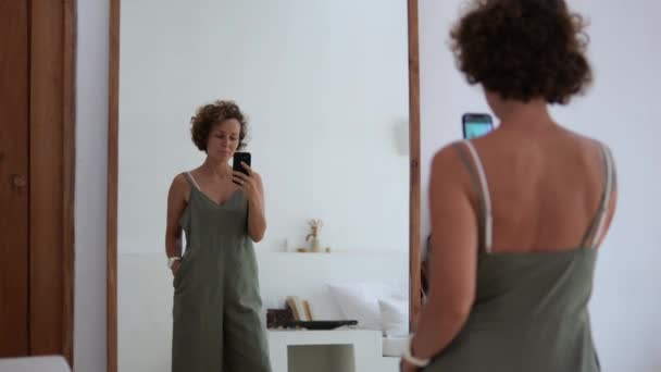 電話で鏡の前の白人女性は 自分自身 彼女の体 体の形や服の写真を撮ります 鏡の前で自撮り 魅力的な女性が写真を撮る 携帯電話のカメラで自撮り リアビュー — ストック動画
