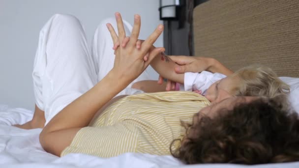 一个有着女婴的慢动作女人躺在床上休息 母亲和孩子手牵手躺在床上 母亲爱孩子 周末和女儿一起休息 妈妈和她的女儿牵着手 — 图库视频影像