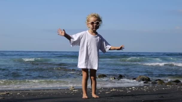 在海滨穿着白色T恤的全长小女孩 周末沐浴在阳光下 可爱的小宝宝站在岸上跳舞很开心 周末假期 快乐的童年在天上美丽的地方 — 图库视频影像